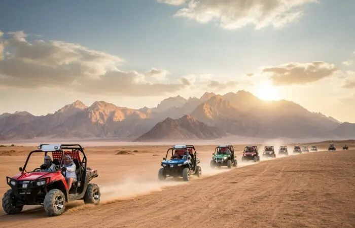 Convoy of 2-seater buggies racing through Sharm El Sheikh's Sinai desert at dusk, kicking up dust with dramatic red rock mountains and hazy skies