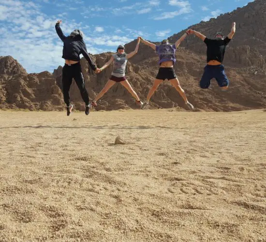 Happy guests beaming with excitement after their desert safari adventure in Sharm El Sheikh, standing in front of quad bikes against the golden Sinai sunset.