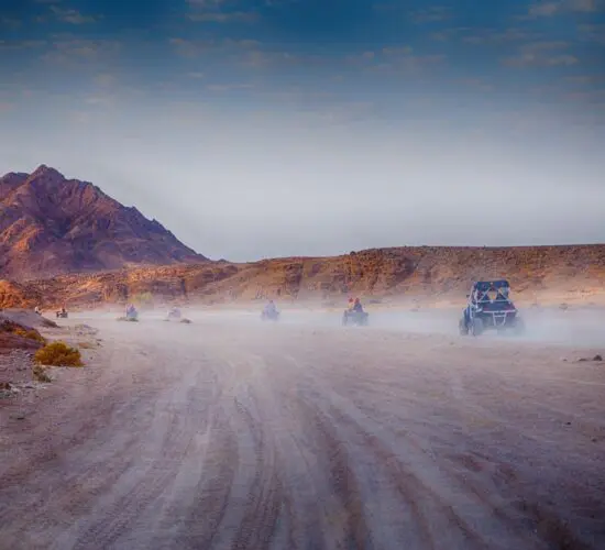 4-seater buggy convoy speeding through Sharm El Sheikh's desert at sunset, kicking up sand with red mountains in the background.
