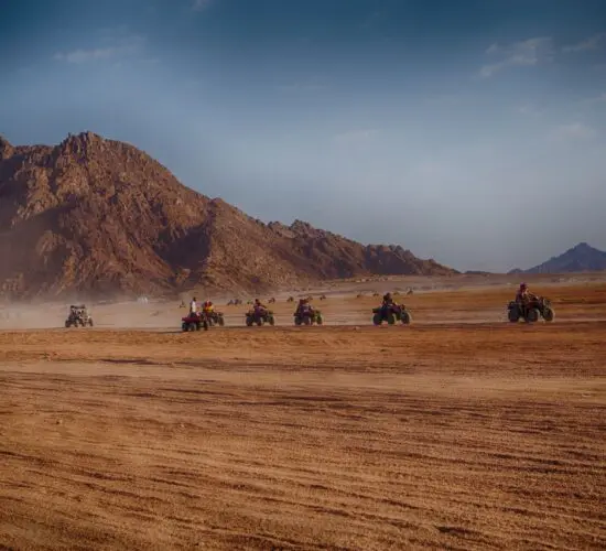 Quad biker powering through the vast Sharm El Sheikh desert at golden hour, sand flying and Sinai mountains glowing in the sunset.