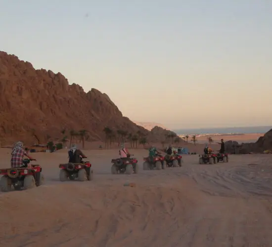 Quad bikers racing through Sharm El Sheikh’s desert at sunset, with dramatic Sinai mountains glowing in golden light.