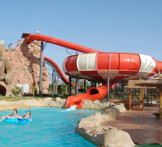 Giant red bowl slide and gorilla-themed rock mountain at Sharm El Sheikh water park, with kids floating in the pool below on a sunny day."