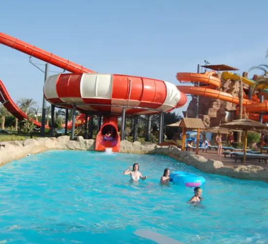 Thrill-seekers flying down the steep blue tunnel slide at Sharm El Sheikh’s water park, splashing into the pool on a sunny day.