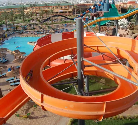 Massive blue multi-lane racer slide at Sharm El Sheikh water park, with excited guests racing down into the splash pool under bright sunshine.