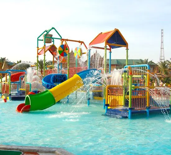 Colorful kids' water play area at Sharm El Sheikh water park, with twisting slides, splashing fountains, and palm trees under sunny skies.